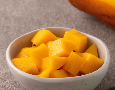 cubos-de-manga-cortada-em-cubos-frescos-sobre-fundo-de-mesa-cinza-com-folhas-tropicais-para-comer_315337-13414